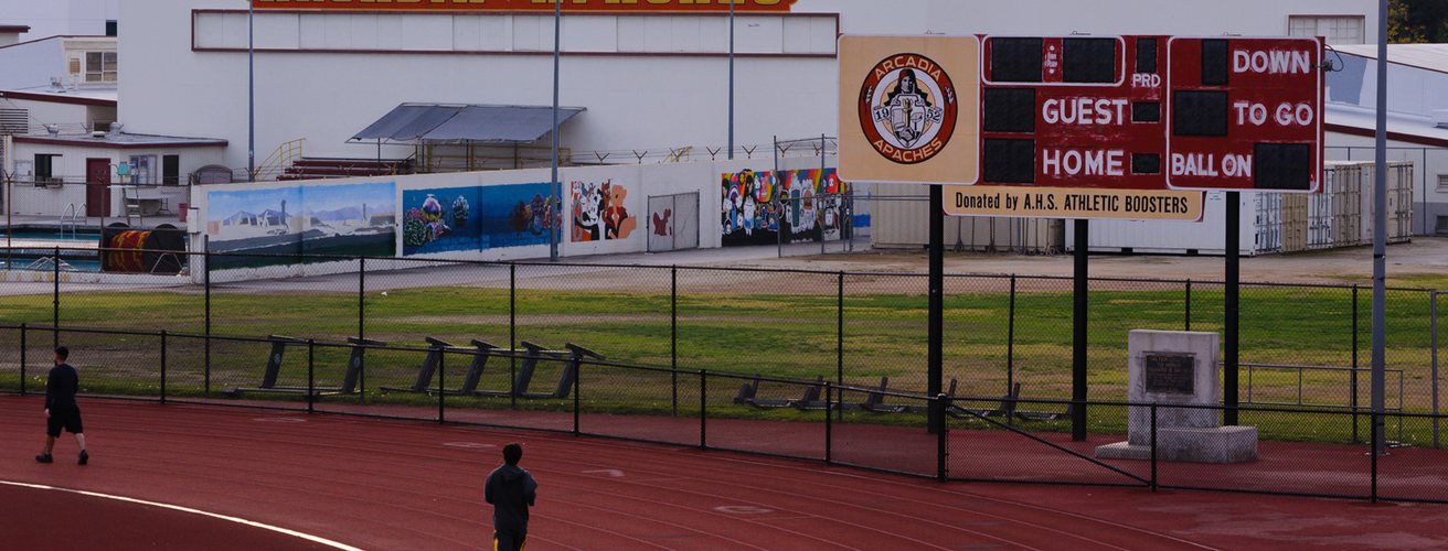 Two runners on an outdoor running track behind a fence