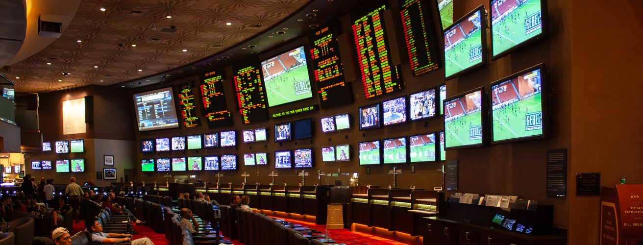 A curved wall of odds screens above the seats of a sportsbook